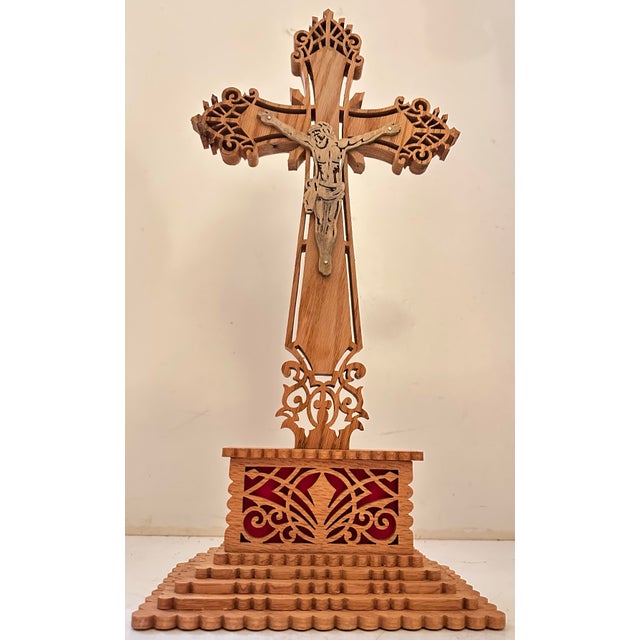 A standing fretwork cross with a carved figure of Christ at the center, mounted on a tiered wooden base. The cross itself...