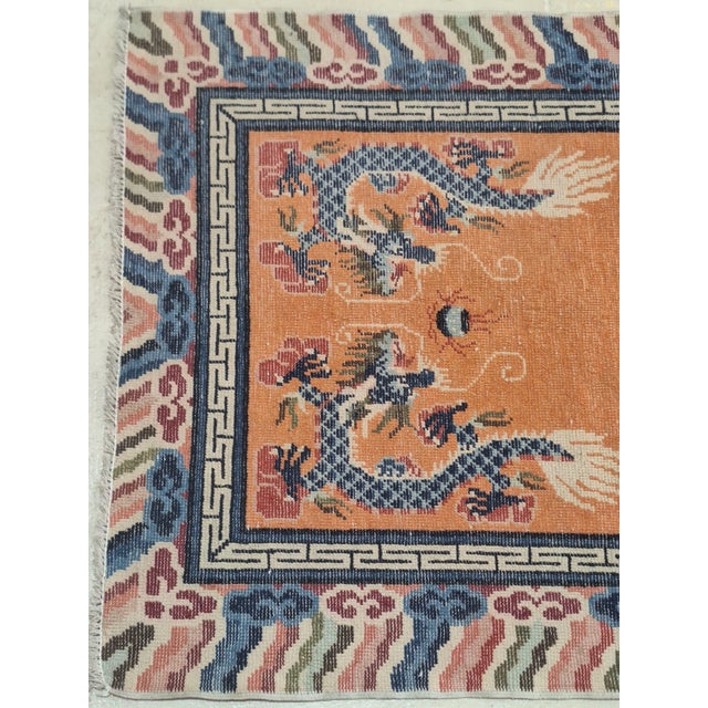 Striking hand-knotted wool rug featuring traditional Chinese dragons chasing flaming pearls across a vibrant saffron...