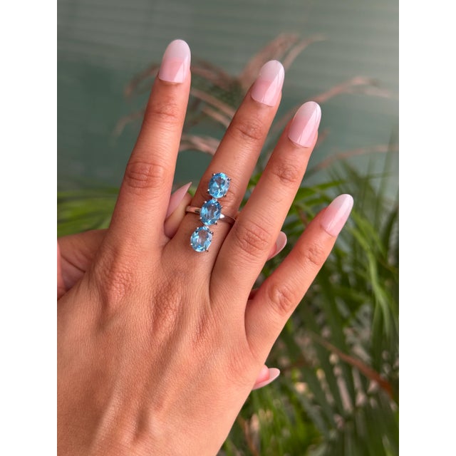 This elegant 925 Sterling Silver ring features a classic three-stone design set with dazzling oval-cut Blue Topaz...