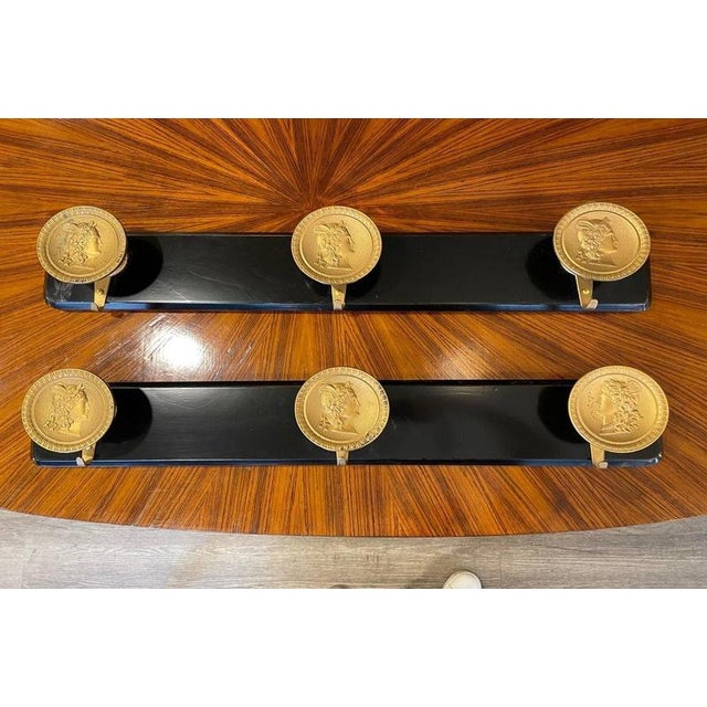 1950s ebonized wood coat rack featuring three brass medallion knobs. Each medallion is decorated with relief portraits of...