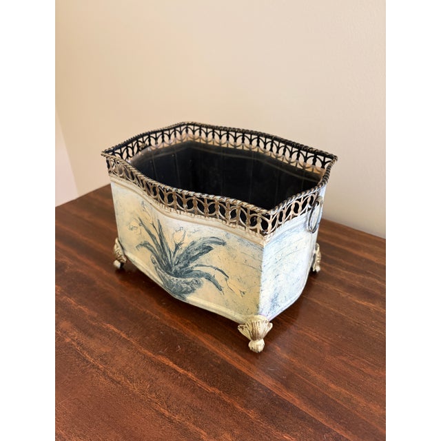 A charming vintage tole cachepot featuring a softly aged cream finish adorned with hand-painted blue tulips in an urn...