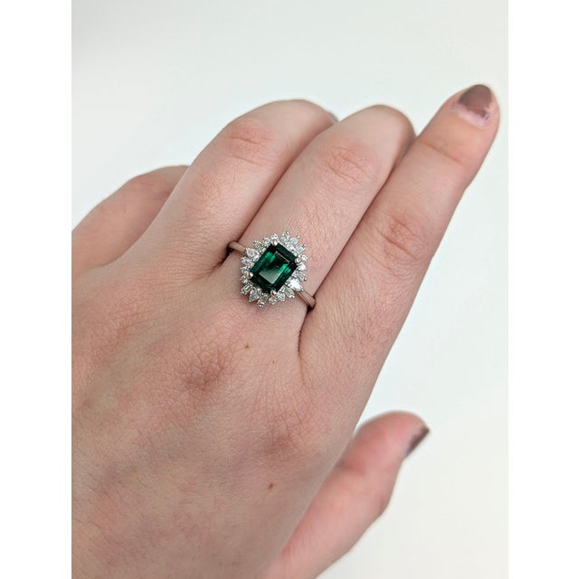A Zambian emerald sits in a lush, forest green at the centre of this solid 14K white gold ring, encircled by twenty earth-...