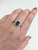 A Zambian emerald sits in a lush, forest green at the centre of this solid 14K white gold ring, encircled by twenty earth-...