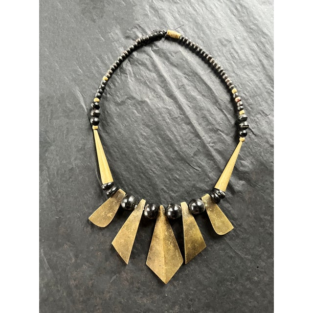 Vintage tribal-inspired necklace featuring shield shaped pendants with exaggerated geometric tapering, interspersed with...