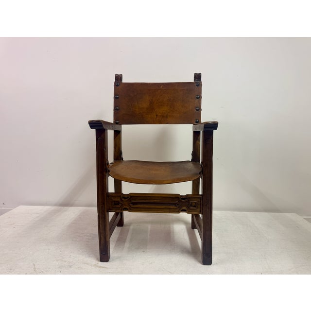 A Spanish armchair dating to the early 20th century, constructed in solid wood with a rich, warm patina and fitted with...