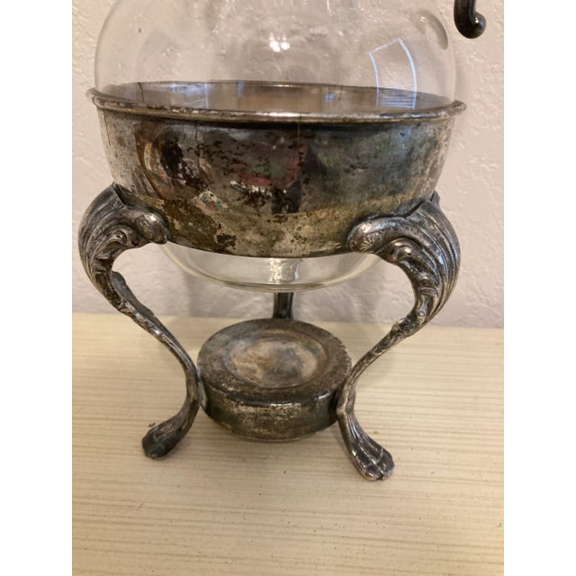 This vintage glass coffee pot is presented in an ornate silver-plate holder featuring scrolling legs and decorative...