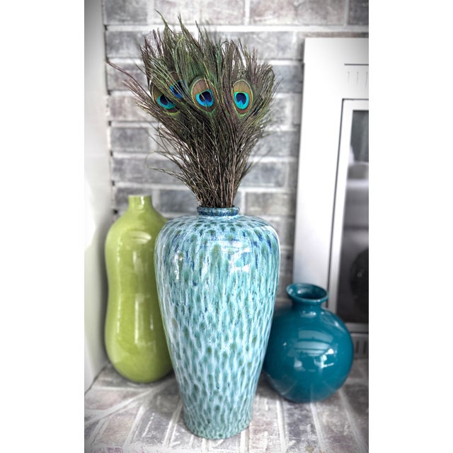 This sculptural ceramic vase features an elegantly tapered form and a luminous, high-gloss glaze inspired by the blues and...