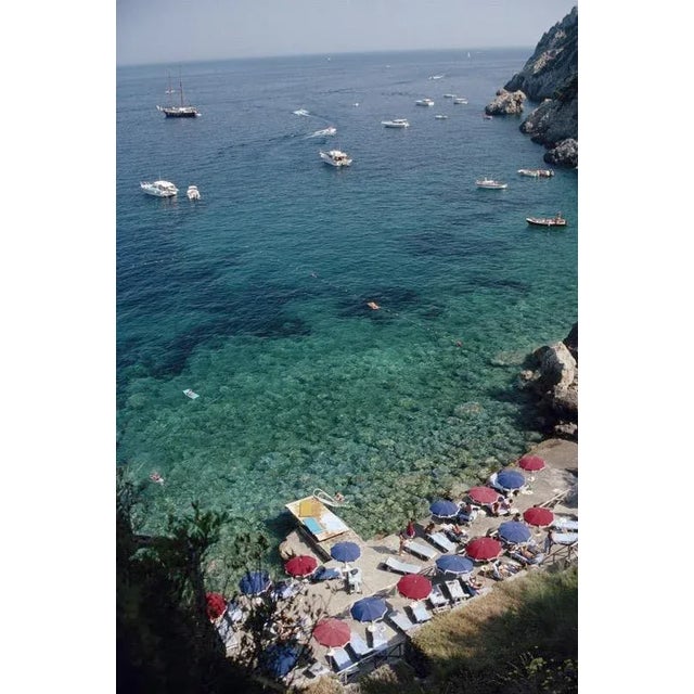 View From Il Pellicano 1991 Aerial view with sunbathers and parasols and, dotted with yachts and small boats, the waters...
