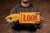 A vibrant hand-painted directional sign used to draw attention toward a nearby coin-operated machine or attraction. The...