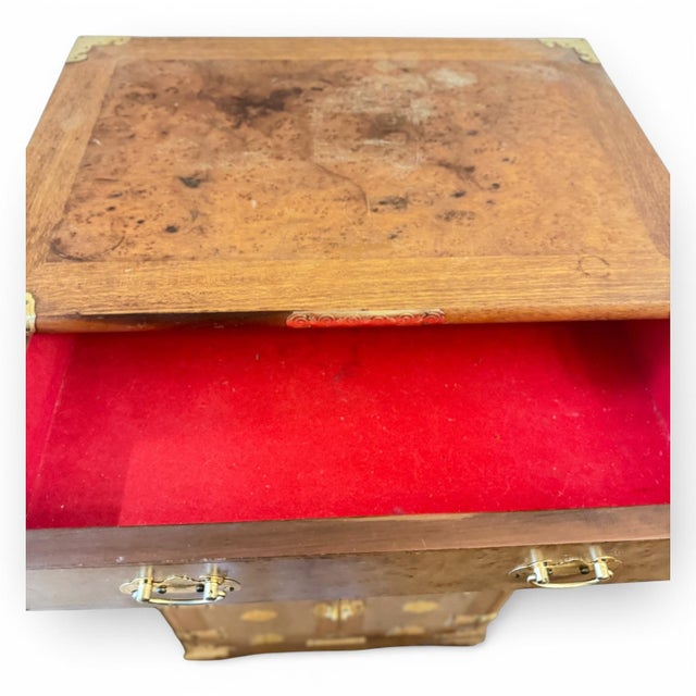 A striking antique English campaign-style chest featuring richly figured burlwood veneer and extensive brass corner mounts...