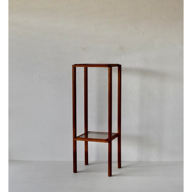 1970s Danish-style pedestal stand crafted from teak wood featuring two smoked glass surfaces. The smoked glass has no...