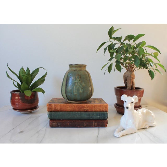 Vintage studio art pottery vessel or vase in greenish blue tones. Features a figure on the front. Signed by the artist on...