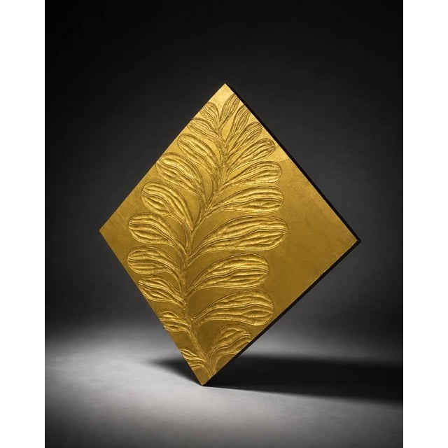 legant square wall plaque featuring a raised botanical leaf relief with a metallic gold finish. The textured surface gives...