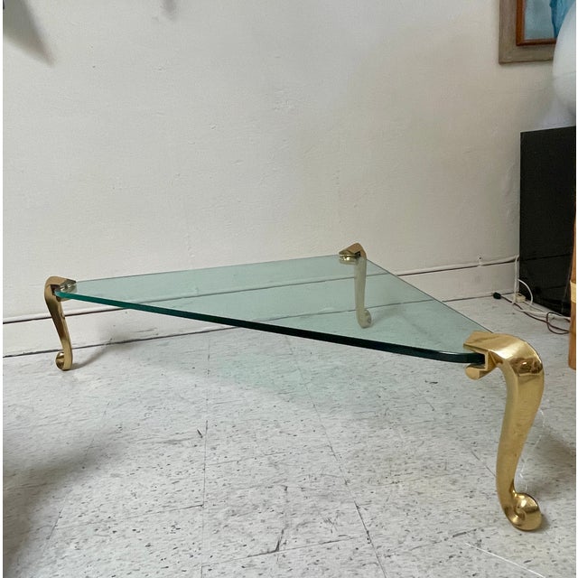 This is a gorgeous vintage coffee table in the Hollywood Regency style. It features a triangular green-tinted glass top...