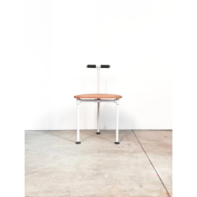 This chair features a structure made of painted iron pipes and fittings, a wooden seat, and plastic/brass terminals.