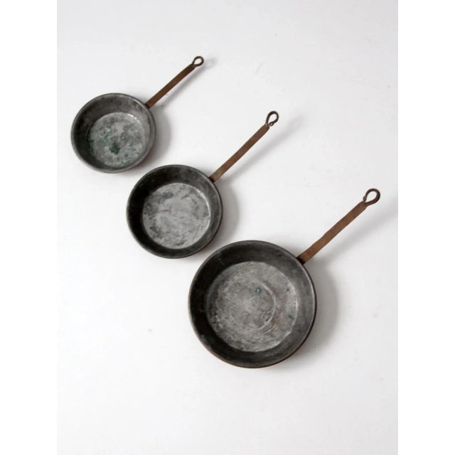This collection of three antique copper sauté pans features classic craftsmanship with warm copper exteriors and...