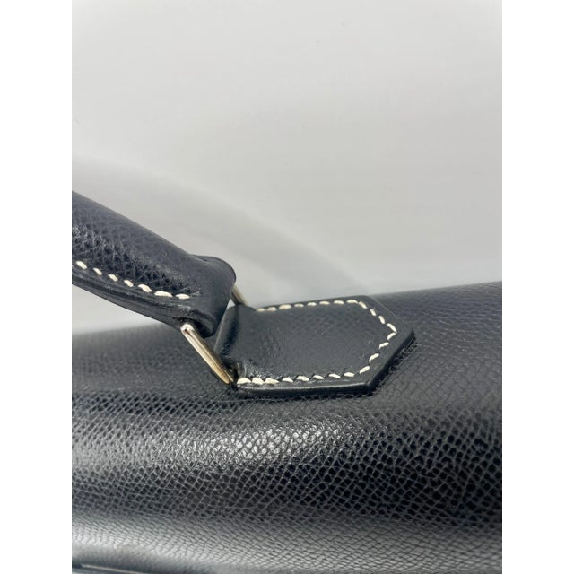 This fashionable handbag is fashioned from supple dark blue calfskin leather. The case has a robust leather top handle...