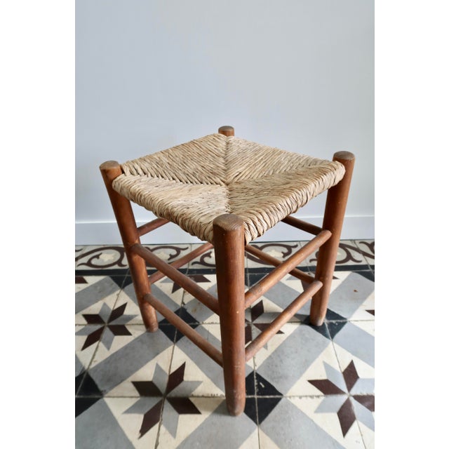 This low vintage stool features a brown-toned wooden frame and a traditional woven straw seat. Its simple silhouette, with...