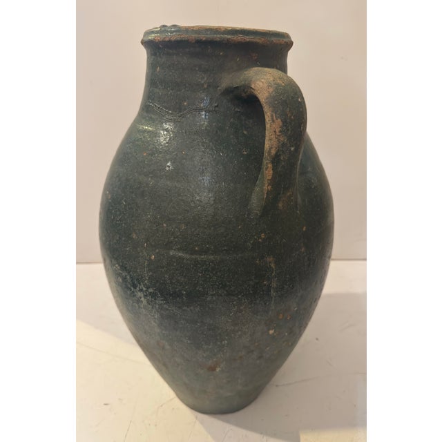 A rustic hand-thrown terracotta amphora with a bulbous body and two loop handles rising from the shoulder to the neck. The...