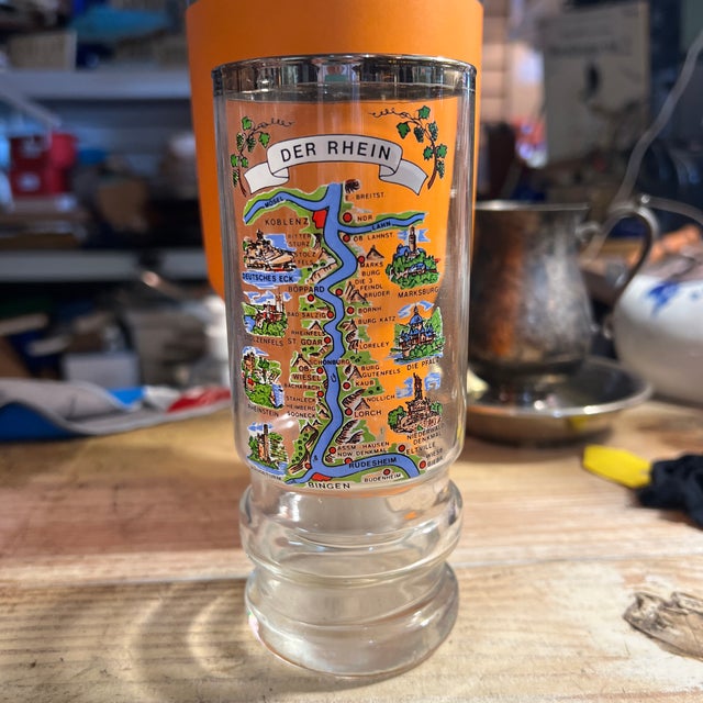 Vintage German glass beer stein featuring a colorful map graphic of the Rhine River (Der Rhein) landmarks. The beer glass...