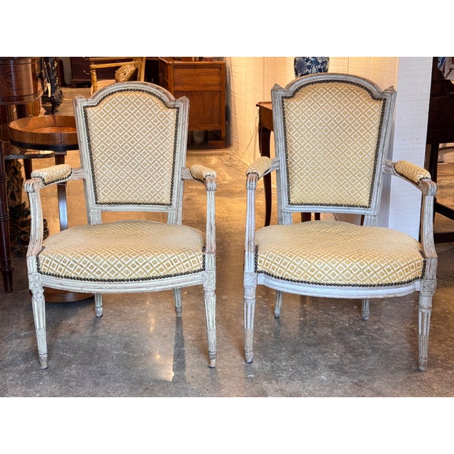 A pair of 19th century French armchairs featuring shaped backs, scrolled arms, and carved floral details throughout. The...