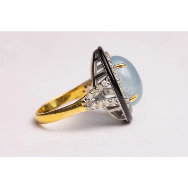 A large oval cabochon aquamarine gemstone bordered in black onyx and round, brilliant cut diamonds in a pave` setting. A...