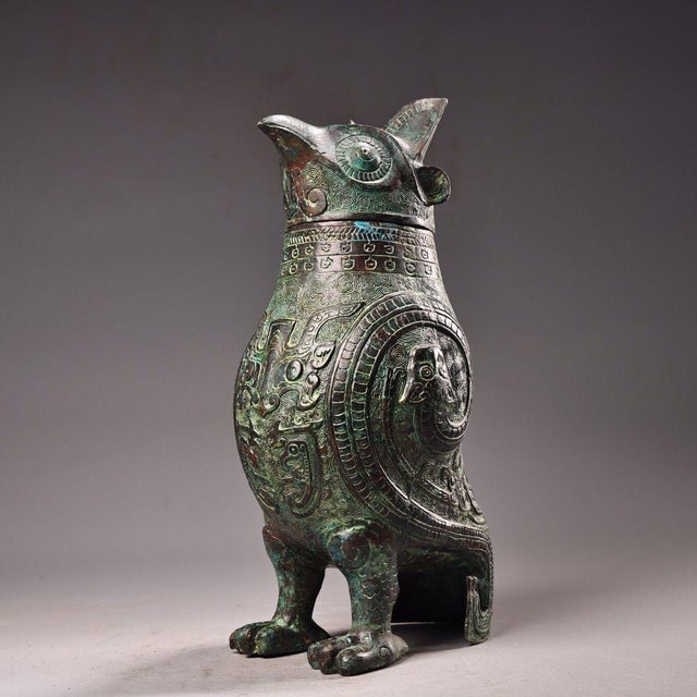 This is a cast bronze ritual vessel in the form of a standing owl, featuring a detachable lid shaped as the bird's head....
