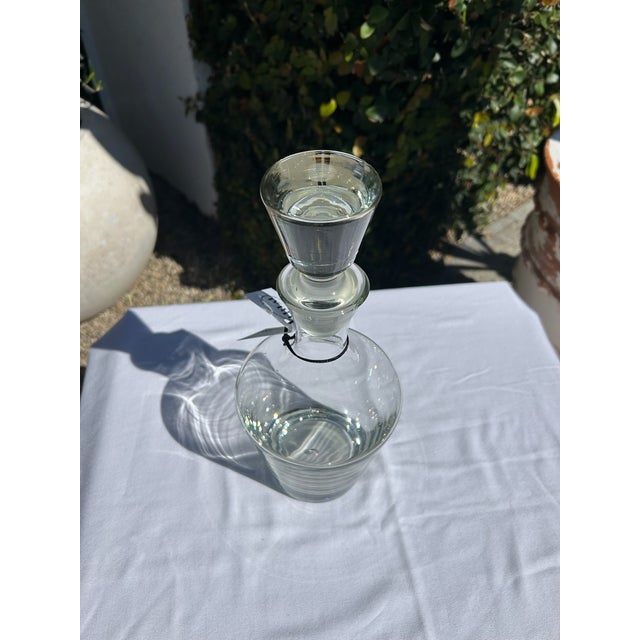 Elegant vintage clear glass decanter featuring a classic silhouette with gently curved body and fitted glass stopper. The...
