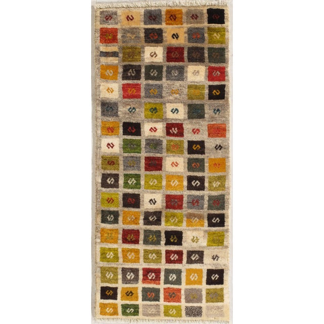 Hand-knotted Persian Gabbeh wool runner featuring a grid of multicolored square motifs on an ivory field. Each square...