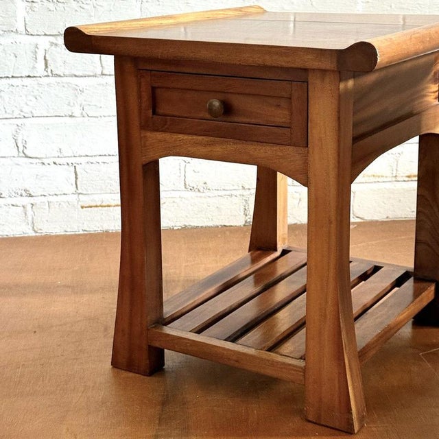 A charming pair of side tables each featuring a single drawer and a slatted lower shelf. The tabletops carry a subtle...