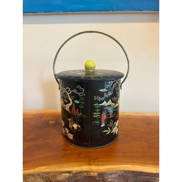 A striking vintage black tea tin featuring detailed Chinoiserie decoration with hand-painted scenic imagery. The design...
