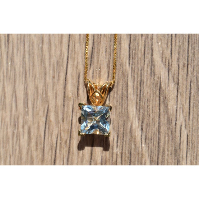The Knoll Court: Princess Cut Aquamarine Pendant in Yellow Gold. The pendant features an elaborate filigree pattern in...