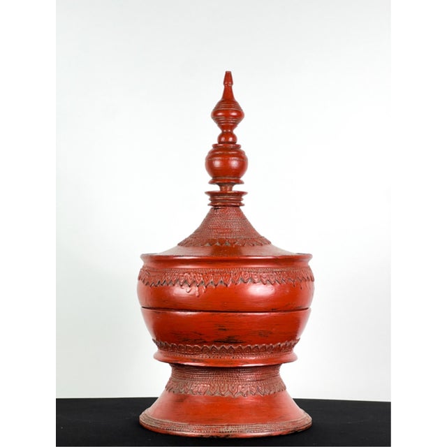 A traditional Burmese deep red three-piece lacquered offering urn with a tall turned finial, domed, spired lid, bulbous...