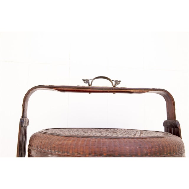 An antique Chinese woven bamboo/rattan wedding basket with a warm honey-brown patina, tall arched bentwood handle with...
