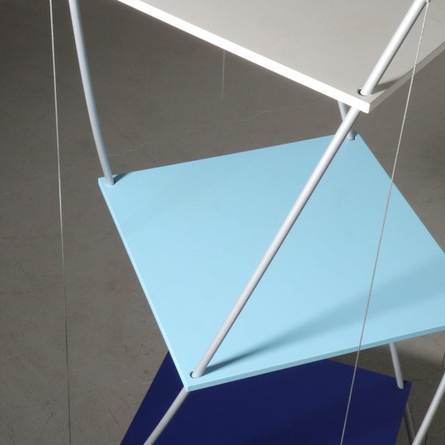 Memphis style etagere or bookcase with steel suspension cables holding it’s form. Three laminate multicolored shelves....