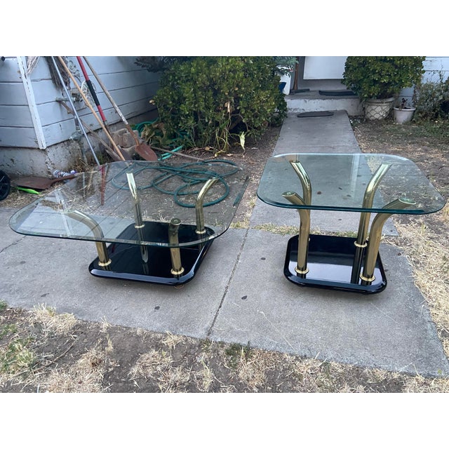 This vintage postmodern Karl Springer style brass tusks coffee table and end table set features a square shape with gold...