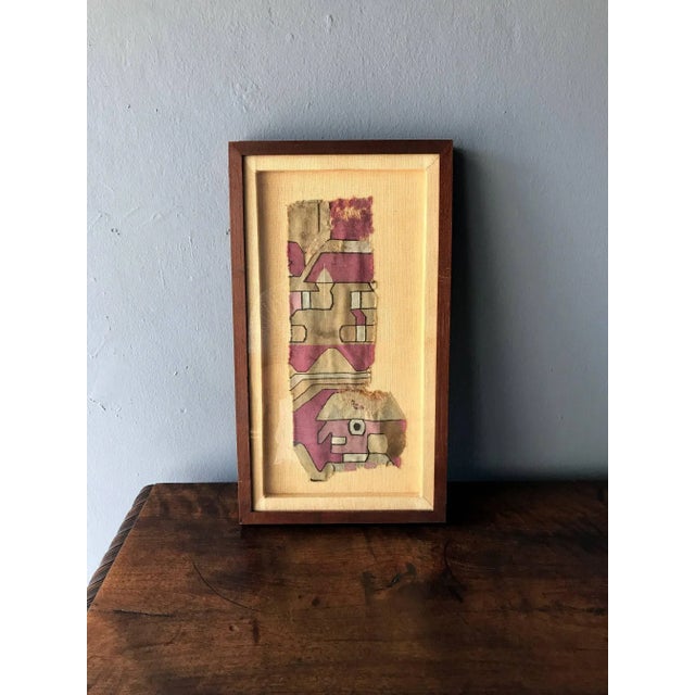 A nicely framed fragment of antique Pre-Columbian textile that depicts a stylized figure in a geometrical background....