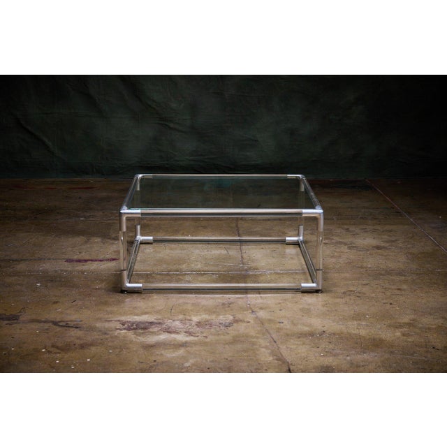 Square chrome and glass coffee table with an acrylic frame. The design has a clean mid century modern look with fitted...