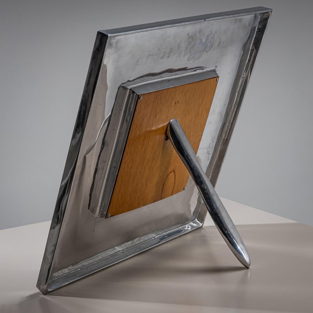 Large tabletop picture frame with a back stand and a wide metal border featuring a slightly convex surface. A decorative...