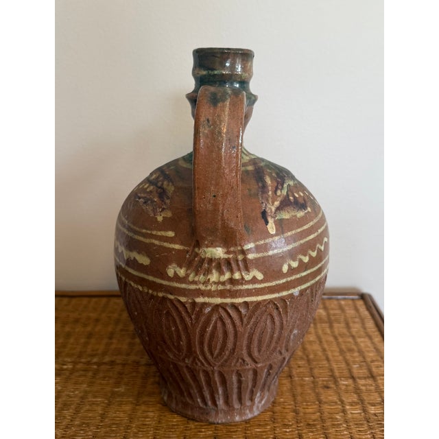 An earthenware ewer with an animal head spout with an open mouth and tooled fur texture. Consistent with rural pottery...