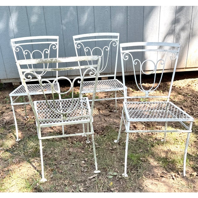 This is a vintage mid-century white wrought iron patio dining chair featuring an ornate scrollwork backrest and a blue...