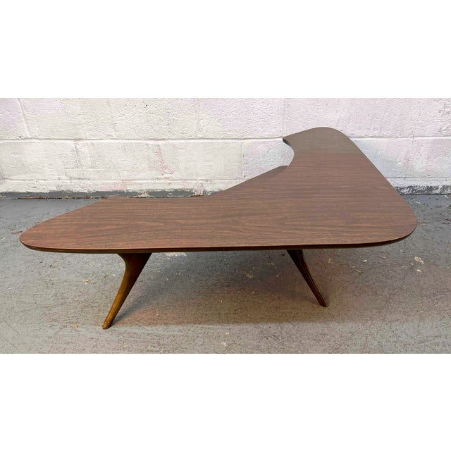 This is a vintage mid-century modern boomerang atomic coffee table featuring a distinctive two-tier wood-grain design and...