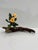 Kindling features a piece of driftwood that serves as a natural base for vibrant yellow flowers, juxtaposed against the...