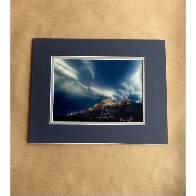 A striking contemporary landscape photograph capturing a rugged mountain peak beneath a dramatic, swirling sky. The...