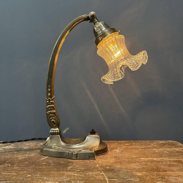 Graceful Art Nouveau table lamp with transparent glass shade from France, around 1920. The skirt-shaped glass shade is...
