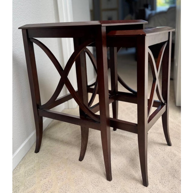 A refined pair of mahogany-finished nesting tables featuring elegant curved X-form stretchers and gently tapered legs. The...