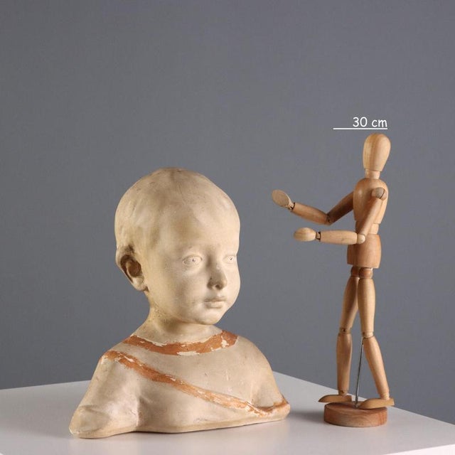 Painted ceramic half-bust depicting an Ancient Greek boy. The artist's initials are engraved under the base. This piece is...