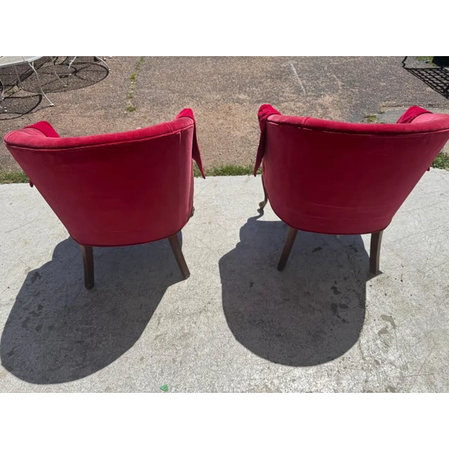 pair of crimson red velvet bergère-style armchairs with carved wooden legs. These chairs are often associated with 19th-...