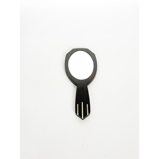 An elegant Art Deco hand mirror crafted from ebonized wood, featuring delicate light-colored Bakelite inlays on the...