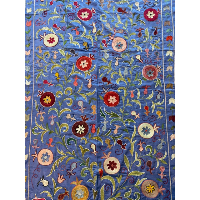 Hand-embroidered Suzani panel from Uzbekistan — red and cream floral rosettes on climbing vines over a cornflower blue...